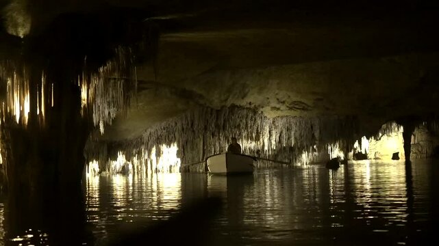 Gondolier rowing a small boat across an underground lake, surrounded by stunning cave formations and serene reflections