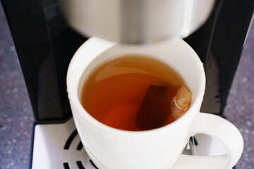 Hot water pours from the thermopot in a cup with a tea bag. household appliance for water heating. Tea and coffee making service. hot water dispenser.