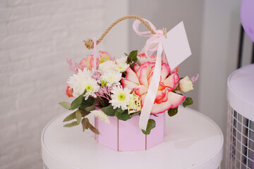 A pink box with a delicate bouquet of flowers on a white round table. A traditional gift for the holiday.