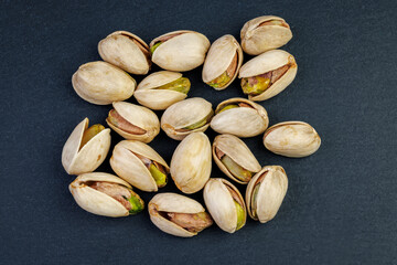 Open pistachios on a dark surface, highlighting their natural texture and vibrant colors.