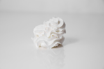 Whipped milk cream from the tube is squeezed onto a white surface. A delicious milk dessert.