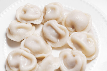 Boiled dumplings are arranged in a circle on a white plate. The plate with dumplings is set against a light background, creating a simple and appetizing composition.