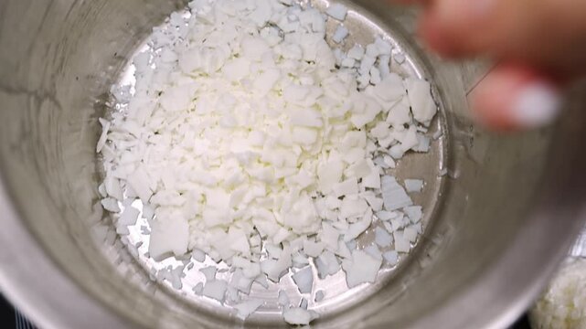 male hand puts soy wax flakes in a saucepan for candle making.