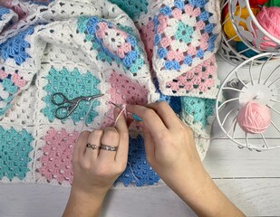 Woman's hands and crocheting process granny square blanket making with clews of yarn and flashlight with candle cozy home photo
