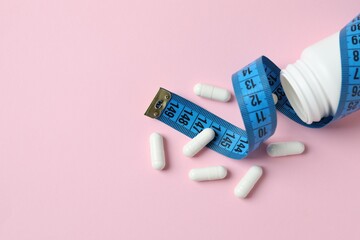 Jar of weight loss pills and measuring tape on color  background, flat lay. Space for text