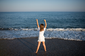 A little girl with her hands up looks at the sea