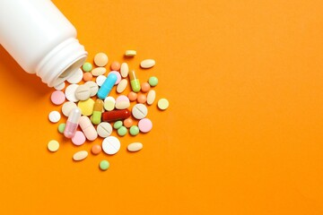 Various pills pouring out of medicine bottle on color background