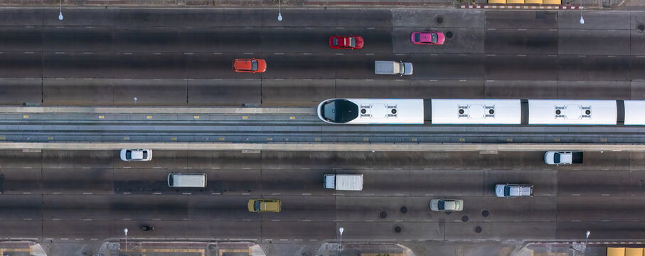 A top-down view of a multi-lane urban road with a central elevated rail track, surrounded by vehicles on both sides, showcasing modern city transportation infrastructure.