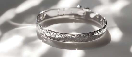 A silver bracelet with elegant engravings placed on a pristine white surface, reflecting bright light and soft shadows. contrast, white background, well-lit, sharp, realistic