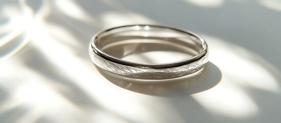 A silver bracelet with elegant engravings placed on a pristine white surface, reflecting bright light and soft shadows. contrast, white background, well-lit, sharp, realistic