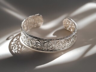 A silver bracelet with intricate details placed on a smooth white surface, illuminated by soft lighting and high clarity. contrast, white background, well-lit, sharp, realistic