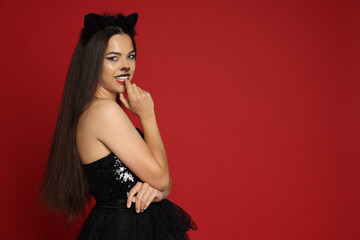 Woman with cat makeup and ears in beautiful dress on red background. Space for text