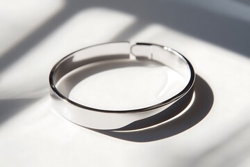A polished silver bracelet with a minimalist design placed on a pristine white surface, casting clear reflections and subtle shadows. contrast, white background, well-lit, sharp, 