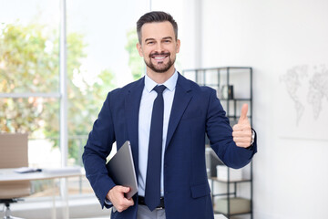 Portrait of smiling banker with laptop showing thumbs up in office