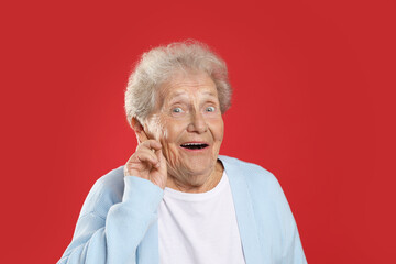 Senior woman showing hand to ear gesture on red background