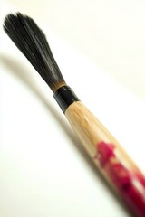 Fototapeta premium A single Japanese calligraphy brush resting horizontally on a clean white surface. The brush has a polished wooden handle and bristles with a slight taper.