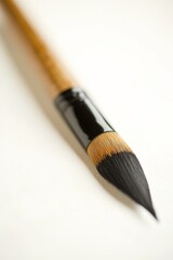 Fototapeta premium A single Japanese calligraphy brush resting horizontally on a clean white surface. The brush has a polished wooden handle and bristles with a slight taper.