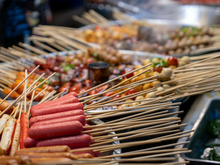 Stewed pot with meatballs and sausages skewers in hot spicy red sauce. Asian street food Thailand.