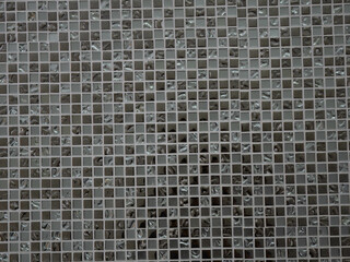 Close-up of a ceramic wall covered with small square mosaic tiles. Classic gray mosaic wall background.