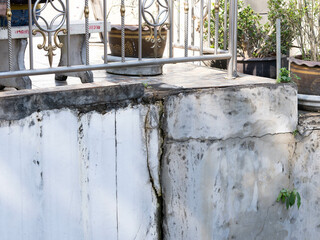Grey cement walls of the house have dark cracks. Cracked concrete wall background.