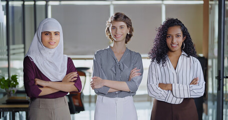 Indian Asian happy young adult gen z proud women lady wear hijab scarf fold hand look cam indoor work place teen mix girls trainee expert female staff group team cross arms do pose job office day