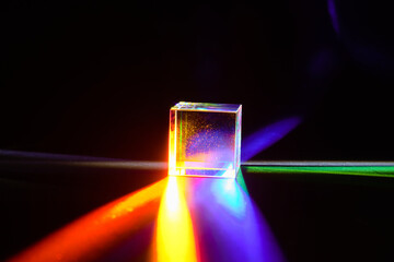 A glass dichroic prism disperse light into different colors on a black background