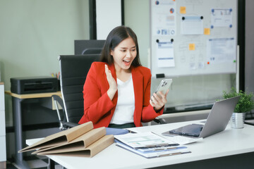 An Asian businesswoman works at her desk in a modern office, smiling while using a tablet to review financial analysis reports, manage accounting tasks, and oversee banking and loan documentation