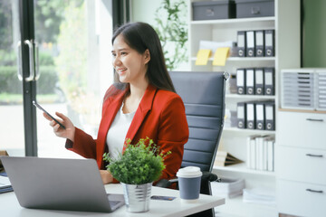 An Asian businesswoman works at her desk in a modern office, smiling while using a tablet to review financial analysis reports, manage accounting tasks, and oversee banking and loan documentation