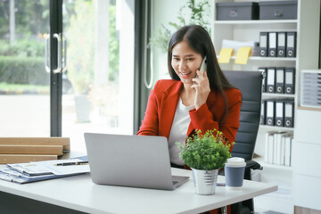 An Asian businesswoman works at her desk in a modern office, smiling while using a tablet to review financial analysis reports, manage accounting tasks, and oversee banking and loan documentation