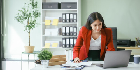 An Asian businesswoman works at her desk in a modern office, smiling while using a tablet to review financial analysis reports, manage accounting tasks, and oversee banking and loan documentation