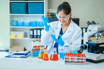 A young female scientist, wearing a lab coat,safety glasses, gloves, examines a test tube containing a lab solution with a microscope,working on a science experiment involving liquid and chemicals