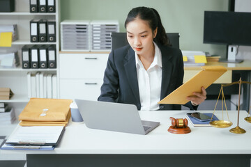 An Asian female lawyer sits at her desk in a modern law office, examining documents meticulously. She shows professionalism and dedication while consulting online and offering legal advice, justice