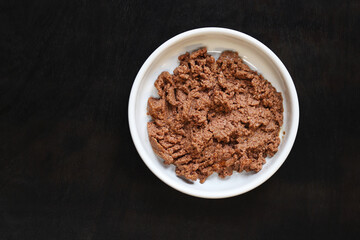 Cat food, pate, top view. Canned food for pets in a round white plate on a dark background. Tasty and healthy food for domestic cats. A portion of wet food, soft pate for a cat on a plate. Copy space
