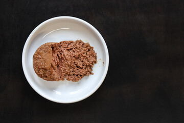 Cat food, pate, top view. Canned food for pets in a round white plate on a dark background. Tasty and healthy food for domestic cats. A portion of wet food, soft pate for a cat on a plate. Copy space