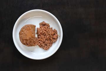 Cat food, pate, top view. Canned food for pets in a round white plate on a dark background. Tasty and healthy food for domestic cats. A portion of wet food, soft pate for a cat on a plate. Copy space