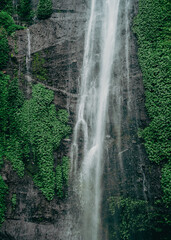 Dramatic waterfall set amidst lush greenery and rocky cliffs, embodying the tranquility and power of nature