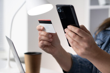 This image shows a closeup view of an individual holding a smartphone in one hand while gripping a credit card in the other, capturing the essence of modern transactions and consumer behavior