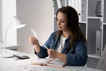 A focused woman meticulously analyzes her receipts at an organized desk, showcasing her attention to detail and highlighting the importance of careful financial management and organization in life