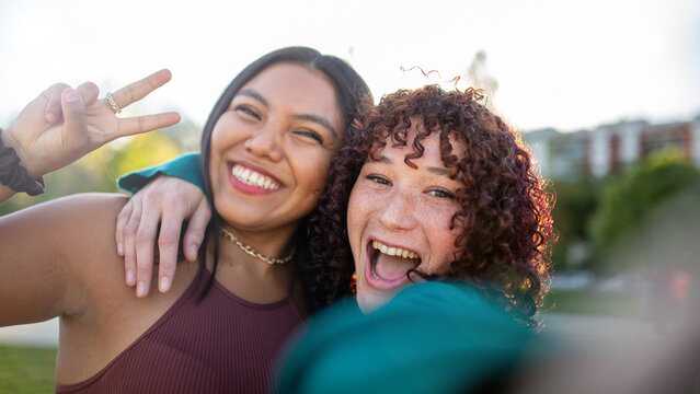 Two women laughing and flashing a peace sign while taking a selfie outdoors