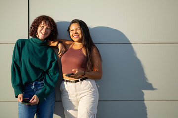 Two friends leaning against a wall and smiling in the sunlight