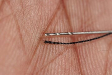 Close-up of a needle threading black thread.  The detail highlights the precision of the task.