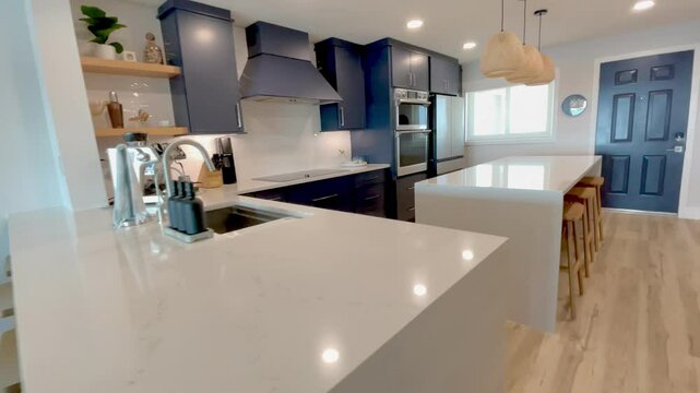 Horizontal video of a modern coastal kitchen in a beachy luxury condo. The newly custom built kitchen features dark blue cabinets, white countertops, and oak wood accents.