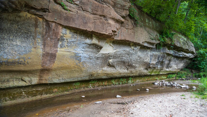 Sandstone ledge colored from water seepage with a creek at the base a nature park in Iowa; concepts of nature lover, tranquility and outdoor adventure
