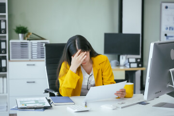 A businesswoman works at her desk in the office, overwhelmed with tasks. She feels tired,...