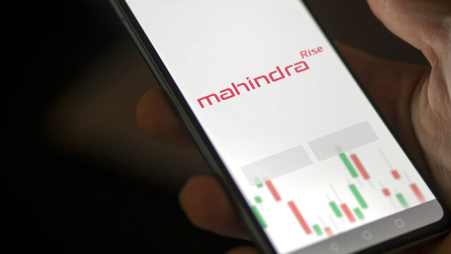 mahindra & mahindra on a screen. A phone shows the prices of Mahindra, An investor analyzing & Mahindra