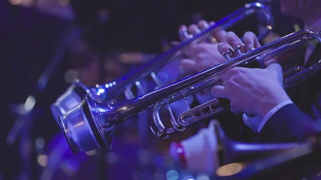 The trumpet section of a big band playing their instruments using cup mutes during a live concert performance in dim stage lights