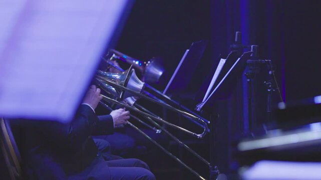 The trombone section of a big band playing their instruments using cup mutes during a live concert performance in dim stage lights. Nr.3