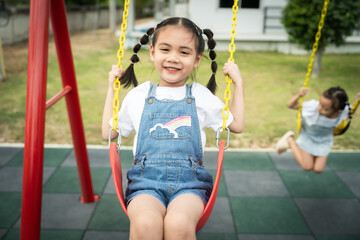 A young girl is swinging on a red swing with a rainbow on it. She is smiling and enjoying herself