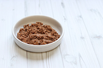 Cat food, pate, side view. Canned pet food in a round white plate on a light wooden background. Tasty and balanced food for domestic cats. Portion of wet food, soft pate for a cat on a plate