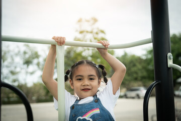 Obraz premium A young girl is hanging from a playground bar. She is smiling and wearing a white shirt with a rainbow on it
